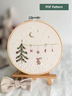 a cross stitch christmas scene with a pine tree and the word noel written in red