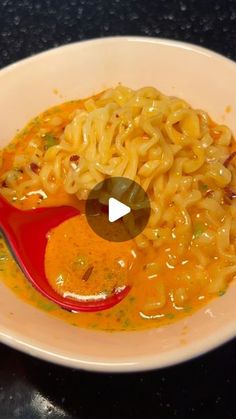 a white bowl filled with noodles and sauce on top of a black table next to a red spoon