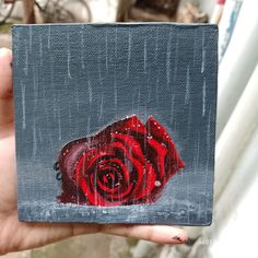 a painting of a red rose on a gray background is being held up by someone's hand