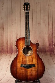 an acoustic guitar sits on a stand against a wooden wall, with the strings still attached