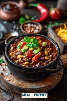 a black pot filled with chili and corn on top of a wooden table next to other bowls