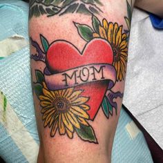 a tattoo on the leg of a person with sunflowers and a heart that says mom