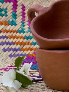 two clay bowls sitting next to each other on a woven tablecloth with white flowers