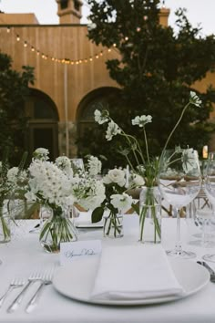 the table is set with white flowers in vases and place settings for two people