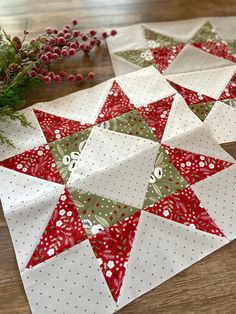 three christmas quilts laid out on a wooden table with pine cones and berries in the background