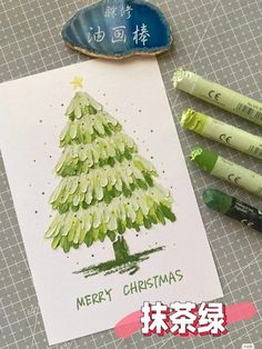 some crayons are next to a christmas card with a pine tree on it