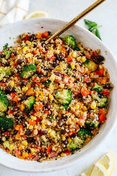 a white bowl filled with rice, broccoli and black beans next to lemon wedges