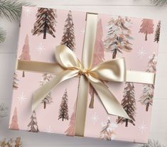 a present wrapped in pink wrapping paper with gold ribbon and pine trees printed on it