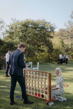 a man and woman playing giant checkers in the grass with other people standing around