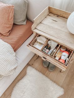 an open drawer on the side of a bed next to a white rug and pillows