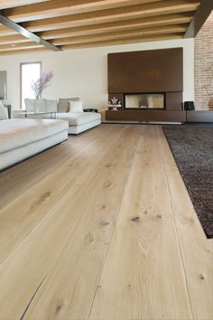 a living room with wood flooring and white couches in front of a fireplace