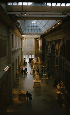 people are walking through an indoor museum with statues on the walls and ceilings, along with large glass windows