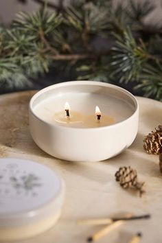 a candle is sitting in a bowl next to some pine cones