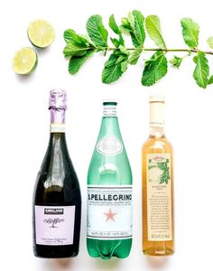 three different types of alcohol on a white surface with green leaves and lemons in the background