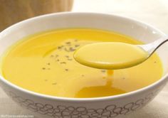 a white bowl filled with yellow liquid and a spoon in the bowl next to it