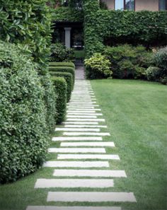 a walkway made out of stepping stones in front of a house with hedges and bushes