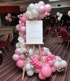 a welcome sign surrounded by pink and white balloons in the middle of a banquet hall