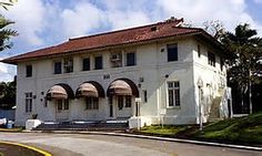 a large white building sitting on the side of a road next to a lush green forest