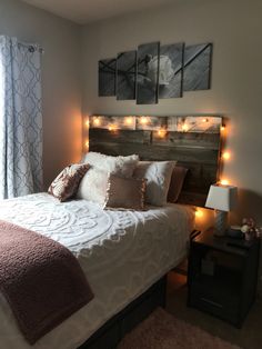 a bed with lights on the headboard and pillows in front of it, next to a window