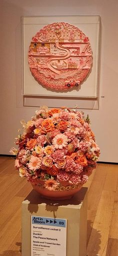 a large vase filled with lots of pink flowers on top of a wooden floor next to a sign