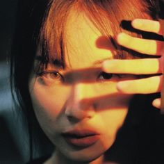 a woman holding her hand up to her face with the sun shining on her face