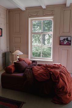 a bed with red sheets and pillows in front of a window