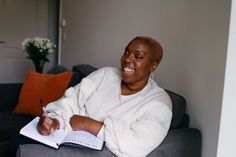 a woman sitting on a couch with a book and pen in her hand while smiling