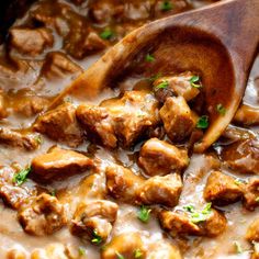 meat and gravy in a white sauce being stirred with a wooden ladle