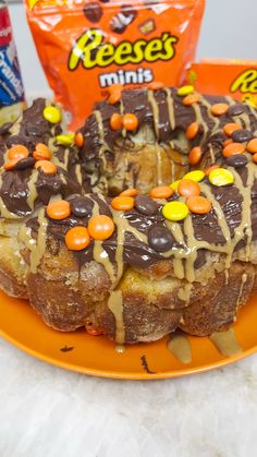 an orange plate topped with a cake covered in frosting and candies next to a bag of reese's minis