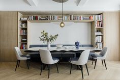 a dining room table with white chairs and bookshelves in the back wall behind it