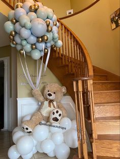 a teddy bear sitting on top of white balloons in front of a stair case and banister