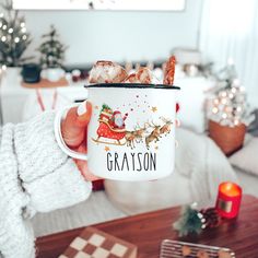 a person holding a coffee mug with food in it and christmas decorations on the table