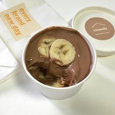 a bowl filled with chocolate and bananas on top of a white table next to a paper napkin