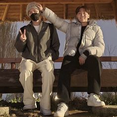 two people are sitting on a bench and one is wearing a mask while the other holds his hand up