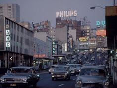 cars are driving down the street in front of tall buildings and neon signs that read phillips