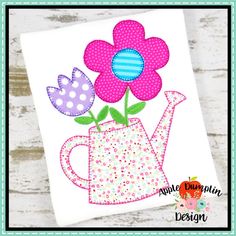 a pink and purple flower in a watering can with polka dot dots on it, next to a white wooden background