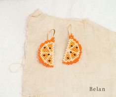 a pair of orange and white beaded earrings on top of a piece of cloth