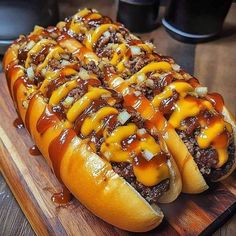 a long hot dog covered in cheese and onions on a wooden cutting board with ketchup