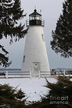 a white light house surrounded by trees and snow