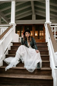 a woman sitting on some steps wearing a white dress and black hat with her hands in her hair