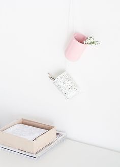 a white desk with a pink flower pot hanging from the wall and a box on top