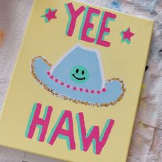 a painted canvas with the words yee haw on it and a blue sombrero