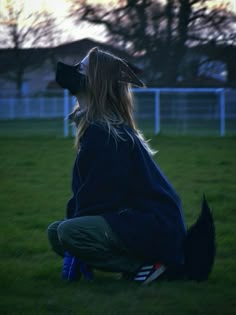 a woman kneeling down in the grass with a bird on her head looking at something