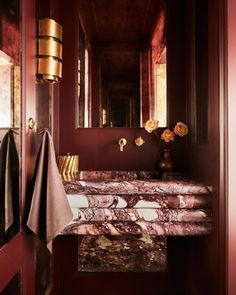 a bathroom with red walls and marble counter tops, gold fixtures and towels on the sink