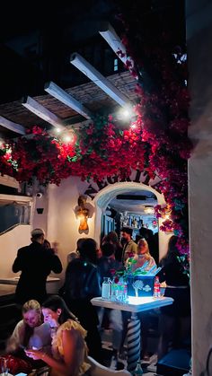 a group of people sitting around a table in a room with flowers hanging from the ceiling