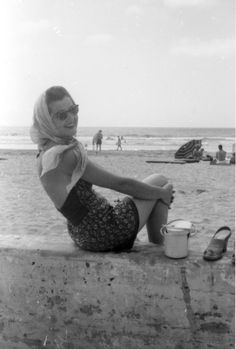 a woman sitting on top of a cement wall near the ocean with her legs crossed