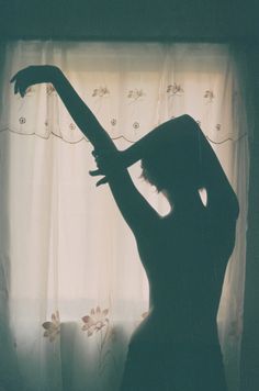 the silhouette of a woman in front of a window with her arm extended and hand over her head