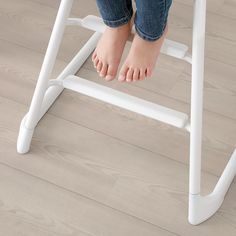 a child's feet sitting on a white stool with wood flooring in the background