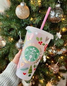 someone holding up a starbucks cup in front of a christmas tree with ornaments on it