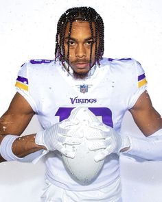 a man with dreadlocks holding a football in front of his face and wearing a white uniform